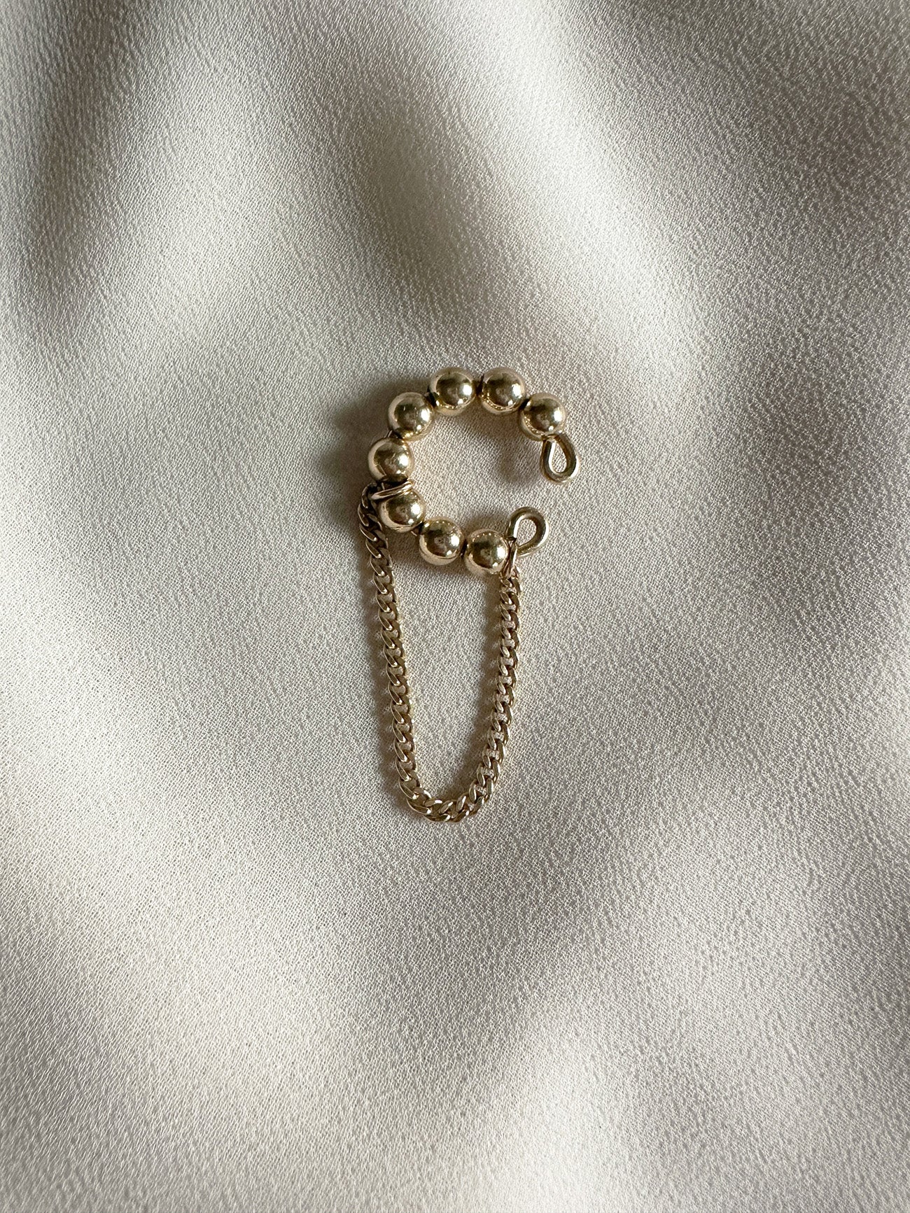 14kt gold filled beaded ear cuff with attached chain dangle, displayed on a soft neutral fabric backdrop.