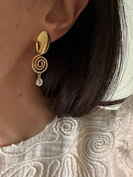 Close-up of an ear with a gold earring and a textured white fabric background.