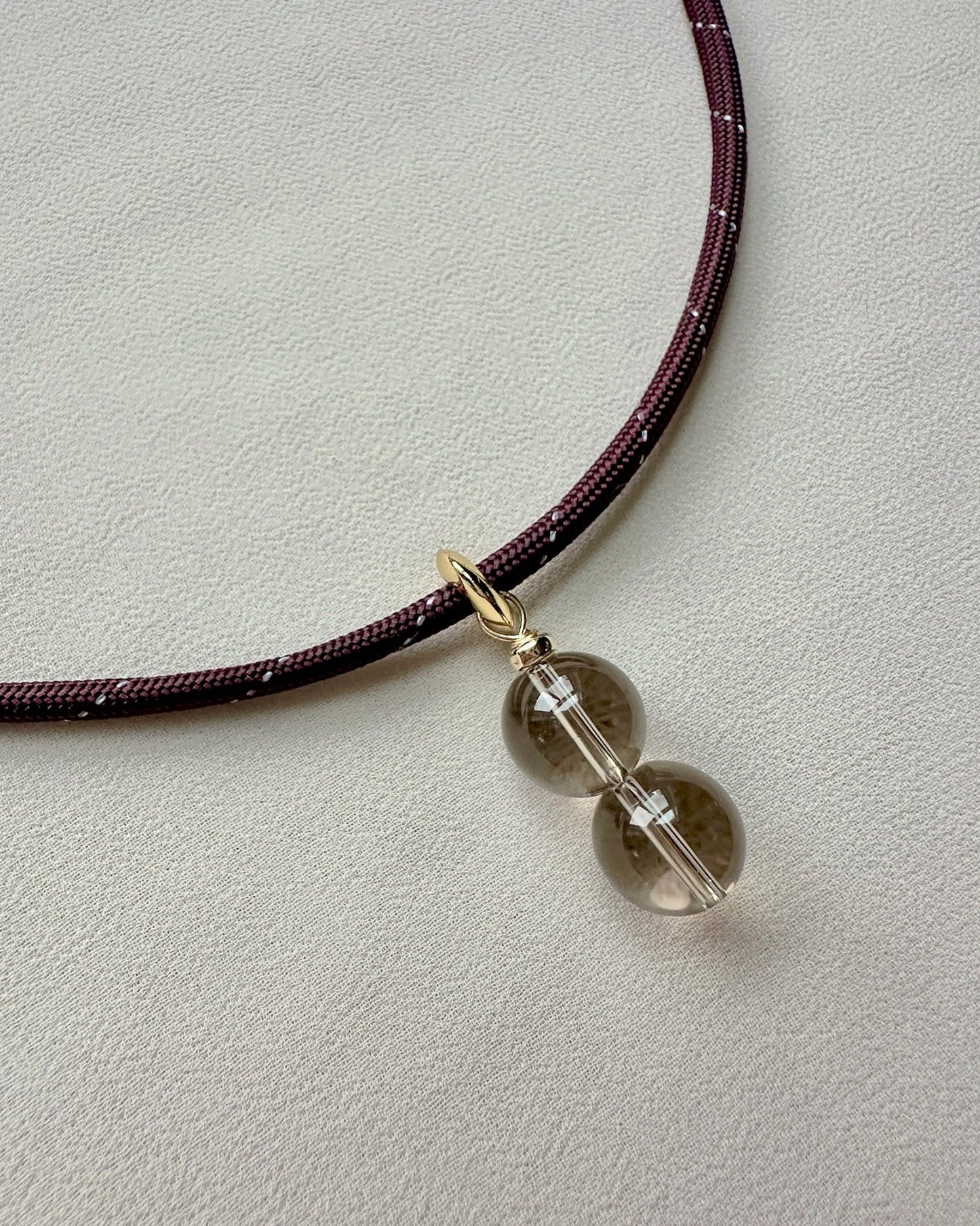 Maroon necklace with a quartz crystal pendant on a light gray background