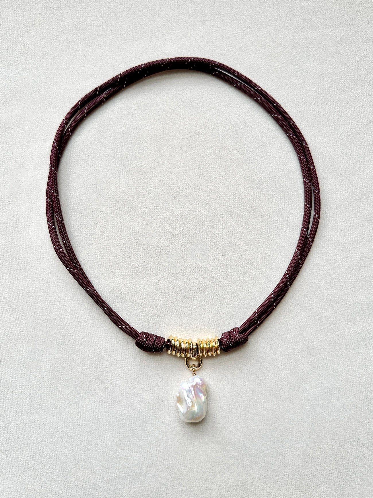 Burgundy paracord, gold and pearl pendant necklace on a white background