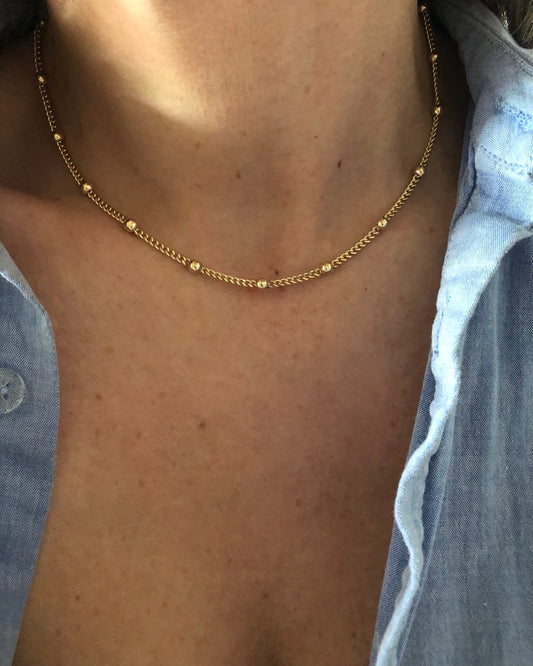 A woman wearing an open blue button up shirt with a studded gold chain necklace.