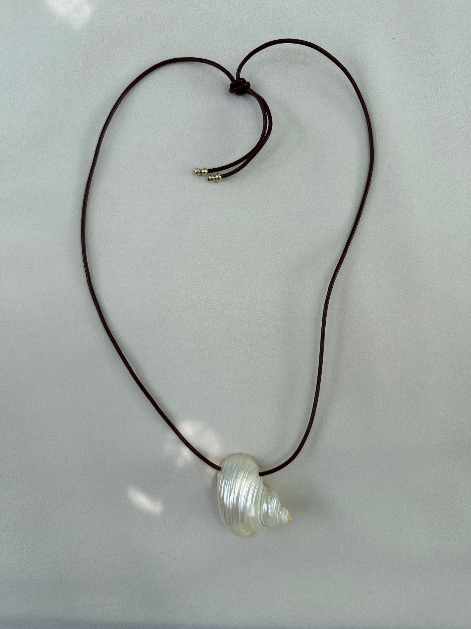 Natural shell necklace on burgundy leather cord flatlay on white packground and sun highlights
