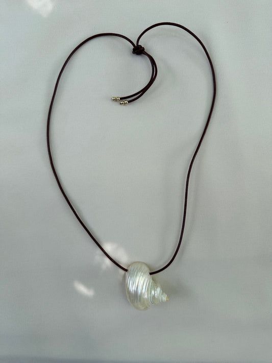 Natural shell necklace on burgundy leather cord flatlay on white packground and sun highlights
