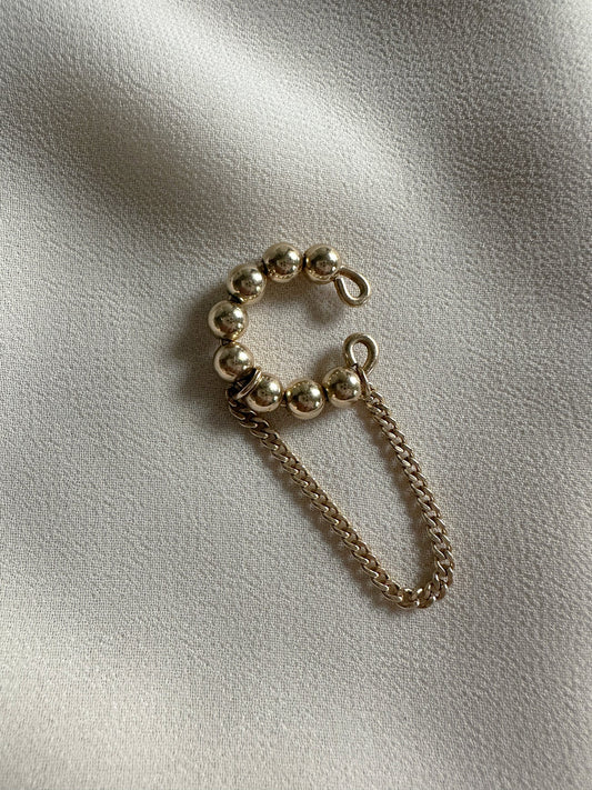 Gold chain and studded bead design earring cuff on a light fabric background