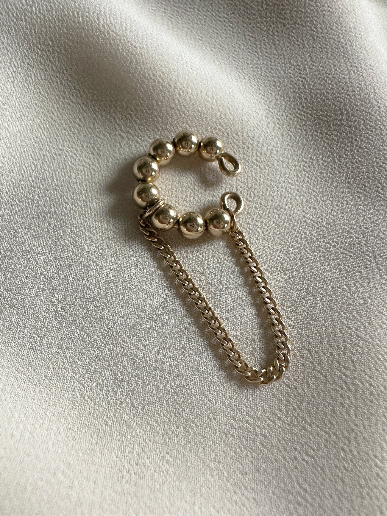 Gold filled beaded ear cuff with attached chain dangle, displayed on a soft neutral fabric backdrop.