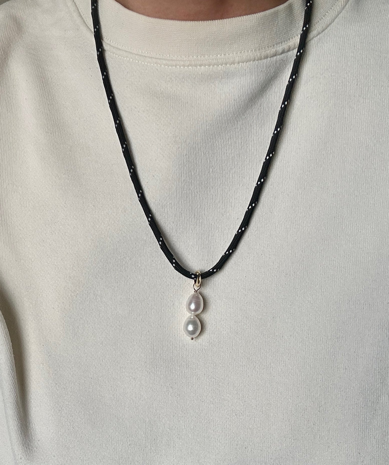 Person wearing a butter yellow jumper and the ELLIOT pearl necklace with a black paracord cord and double freshwater pearl pendant on a gold plated bail.