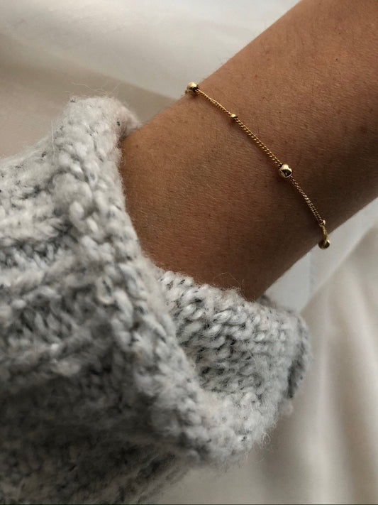 Gold dainty bracelet on a wrist with a blurred background