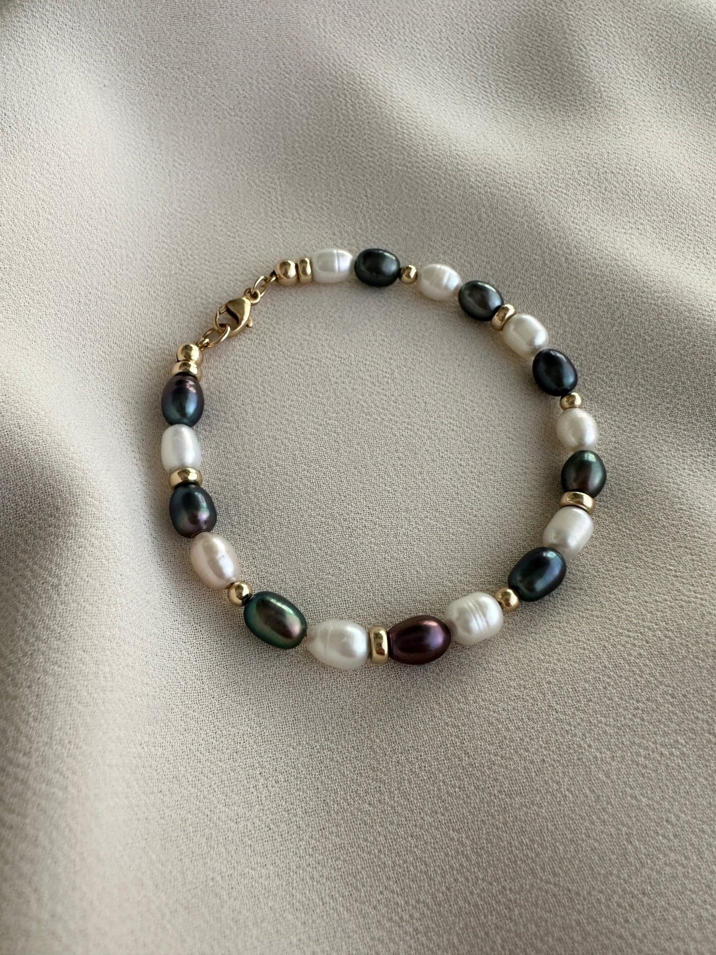 Black and white striped pearl bracelet with gold-filled details on a beige fabric background 
