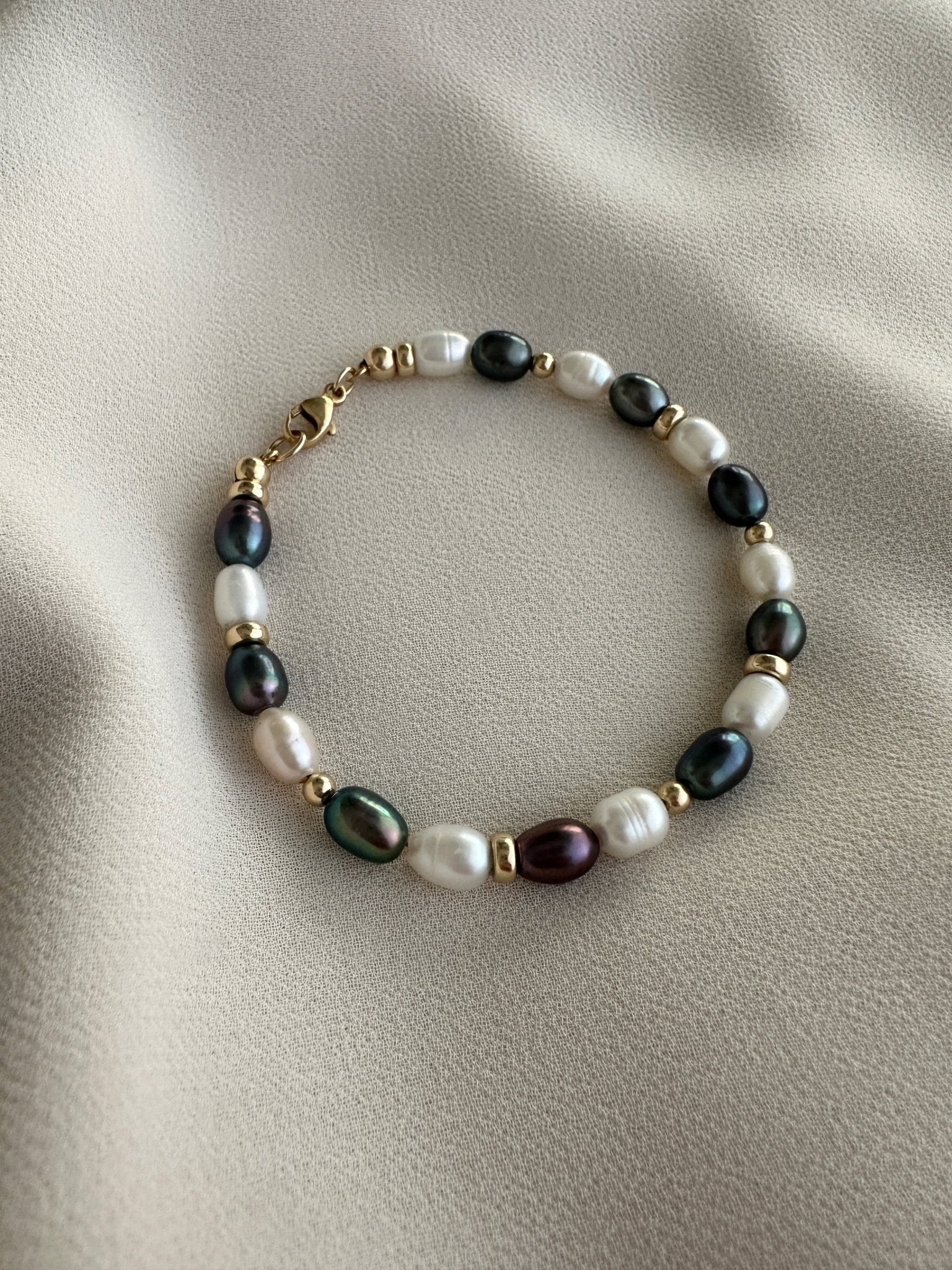 Black and white striped pearl bracelet with gold-filled details on a beige fabric background 