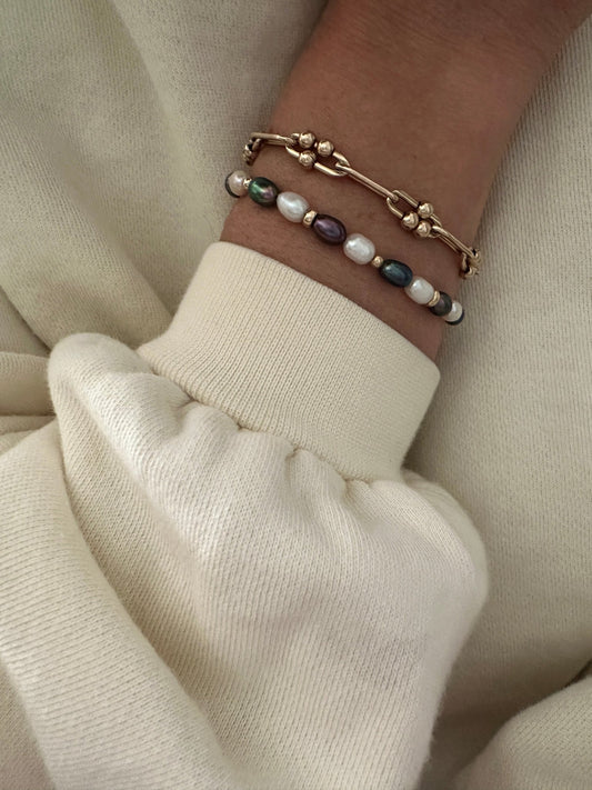 close-up of freshwater pearl and gold-filled chain bracelets on a wrist wearing a cream white shirt
