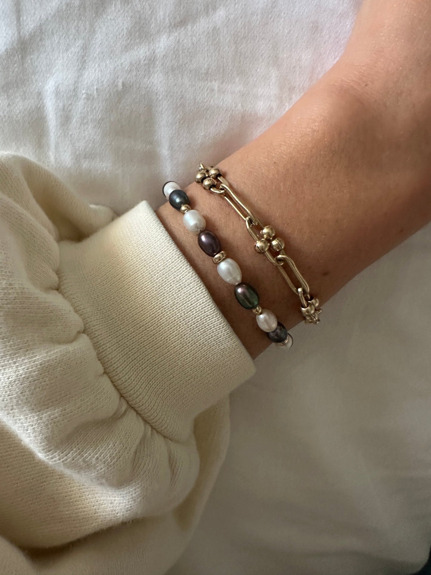 Close-up of a wrist wearing multiple pearl and gold-filled bracelets on a white background
