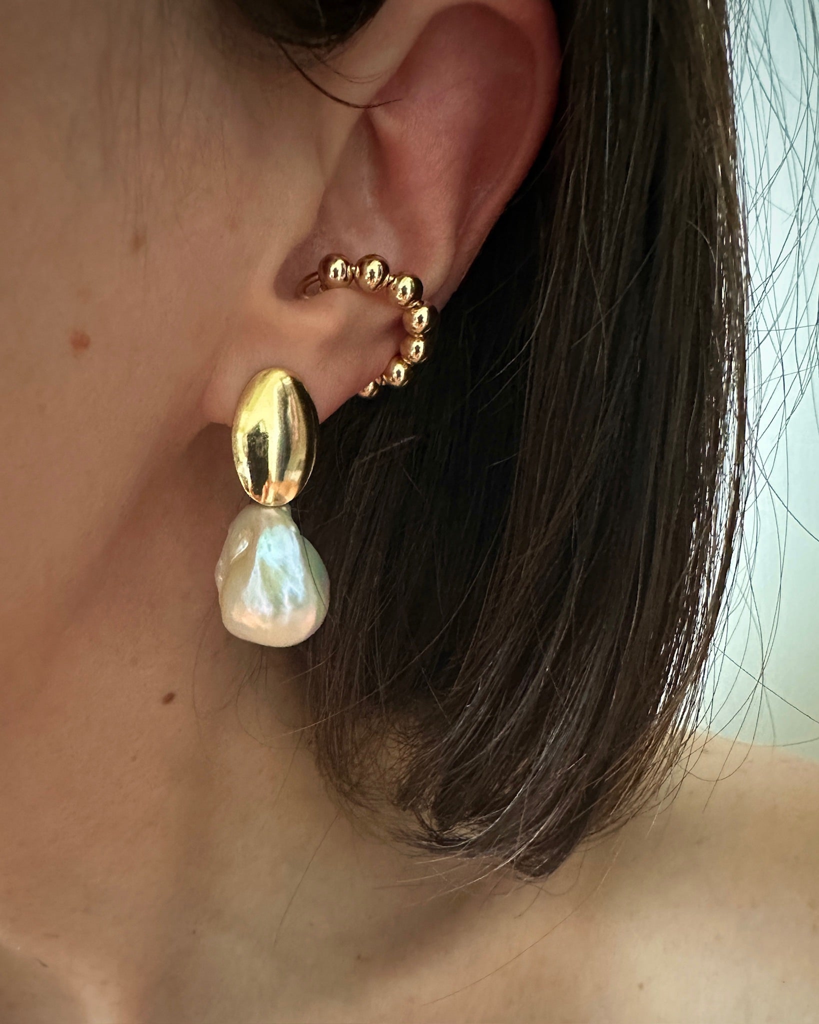 close up of worn pearl and gold earrings with a gold studded ear cuff