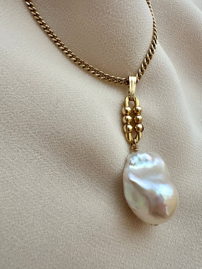 Gold necklace with a large pearl pendant on a beige fabric background