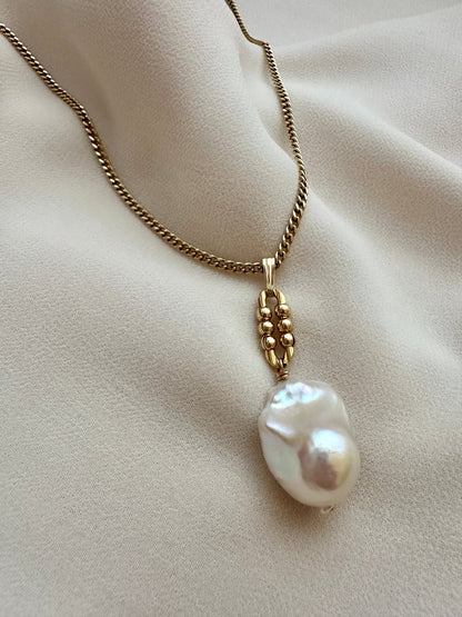 Gold chain necklace with a large pearl pendant on a beige fabric background