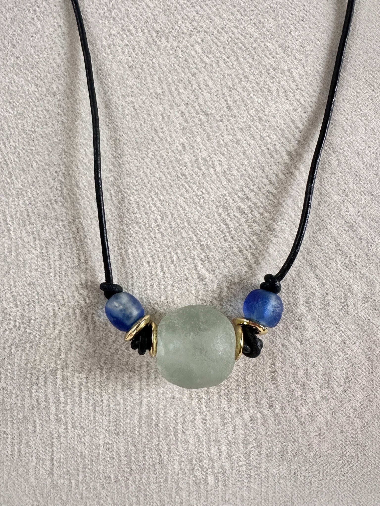 Necklace with a green and blue glass beads on a black leather cord on a light gray background