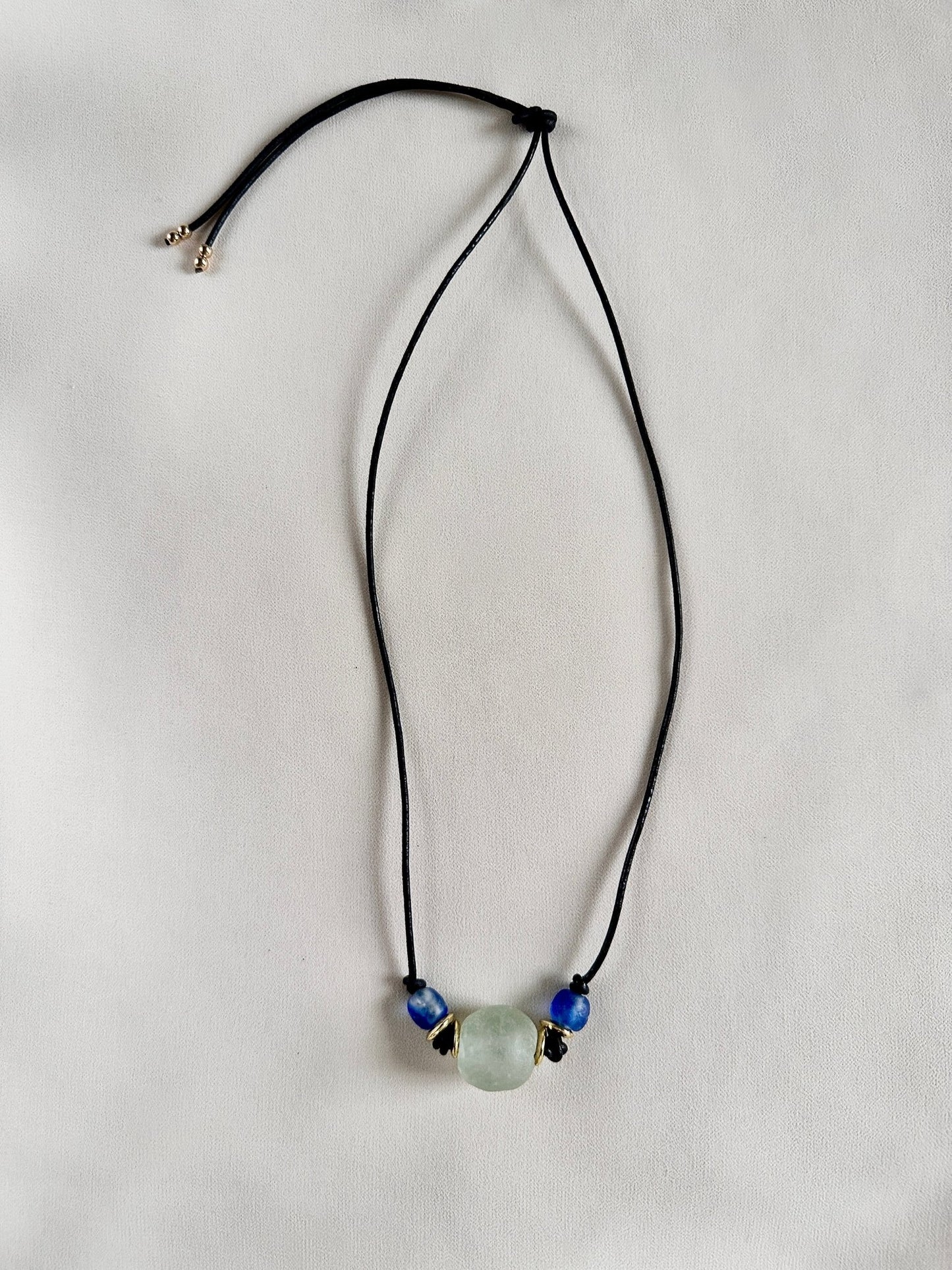 Necklace with a green and blue glass beads on black leather cord on a white background