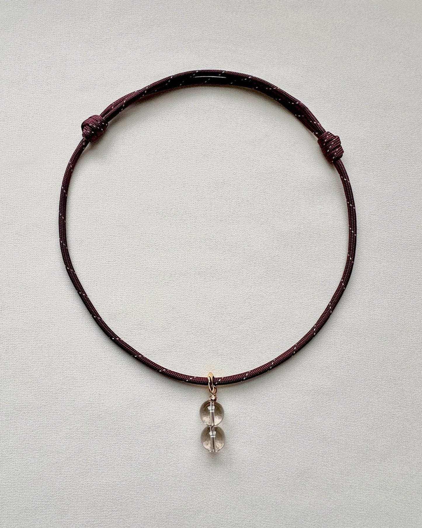Burgundy paracord necklace with a crystal pendant on a light gray background