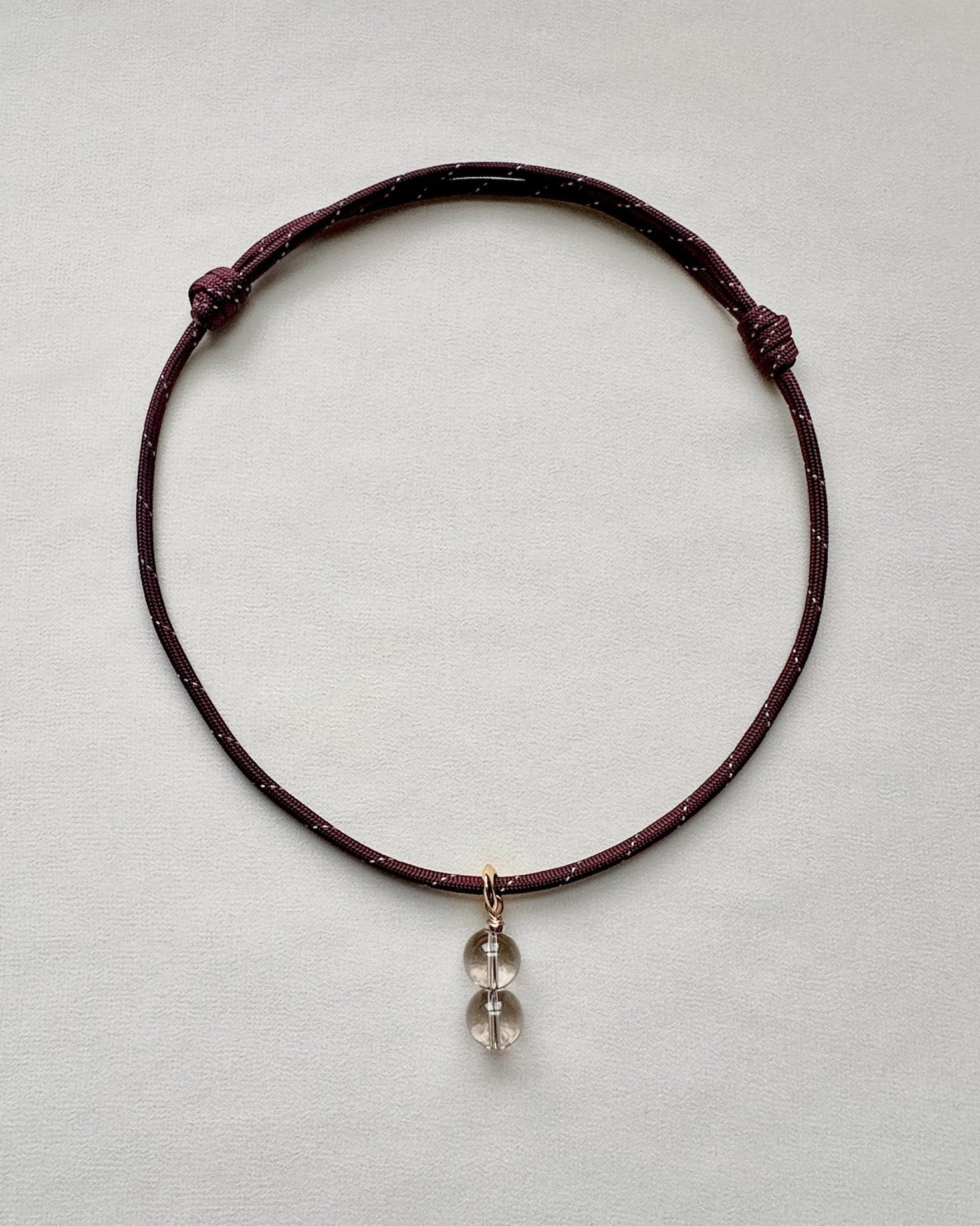 Burgundy paracord necklace with a crystal pendant on a light gray background
