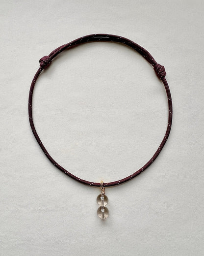 Burgundy paracord necklace with a crystal pendant on a light gray background