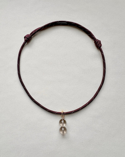 Burgundy paracord necklace with a crystal pendant on a light gray background