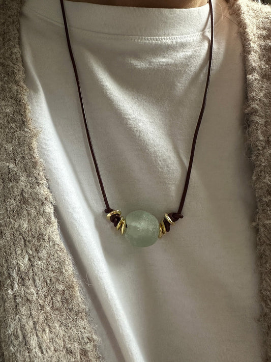 Leather cord necklace with a green pendant on a white t-shirt