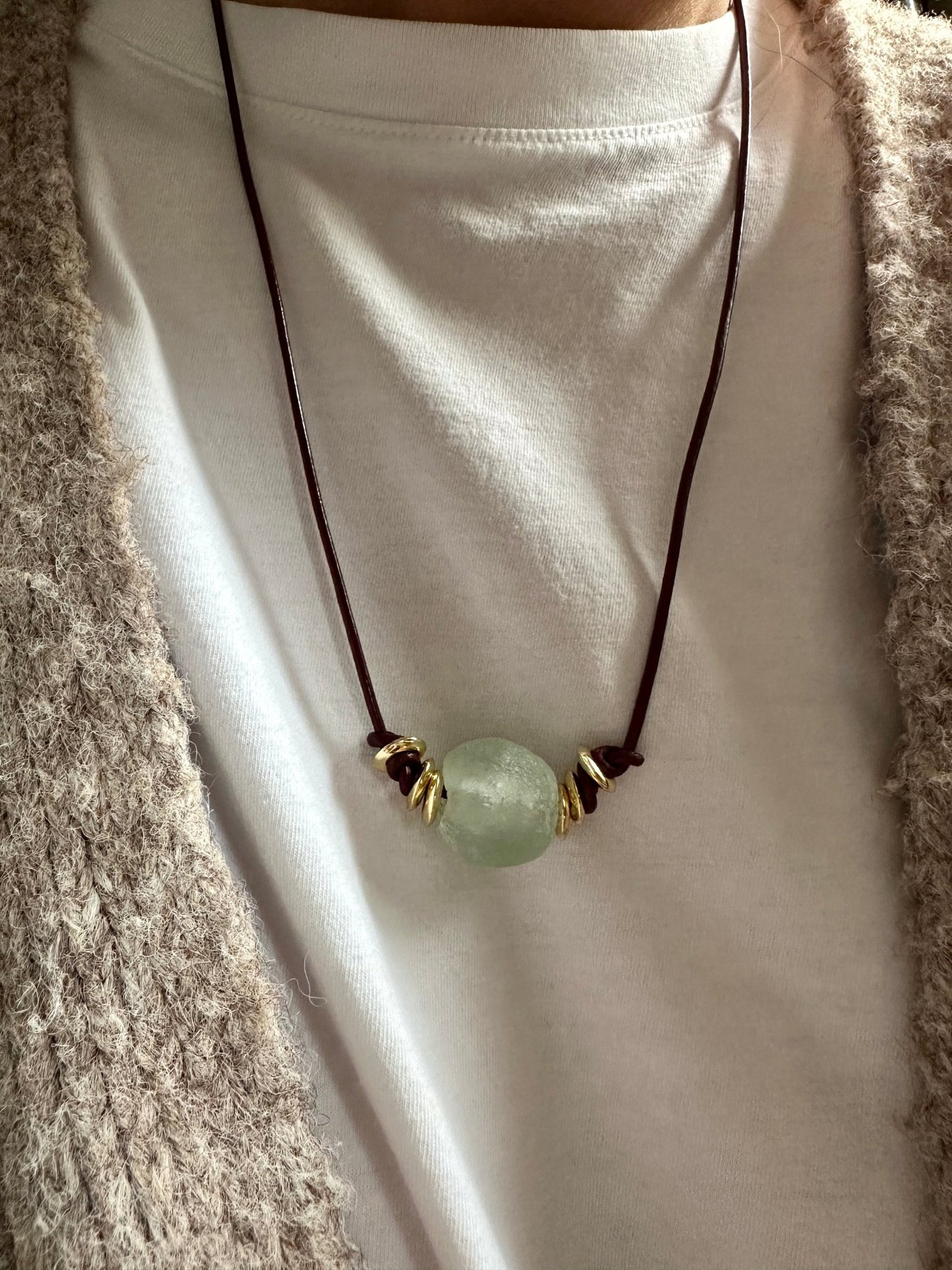 Leather cord necklace with a green pendant on a white t-shirt