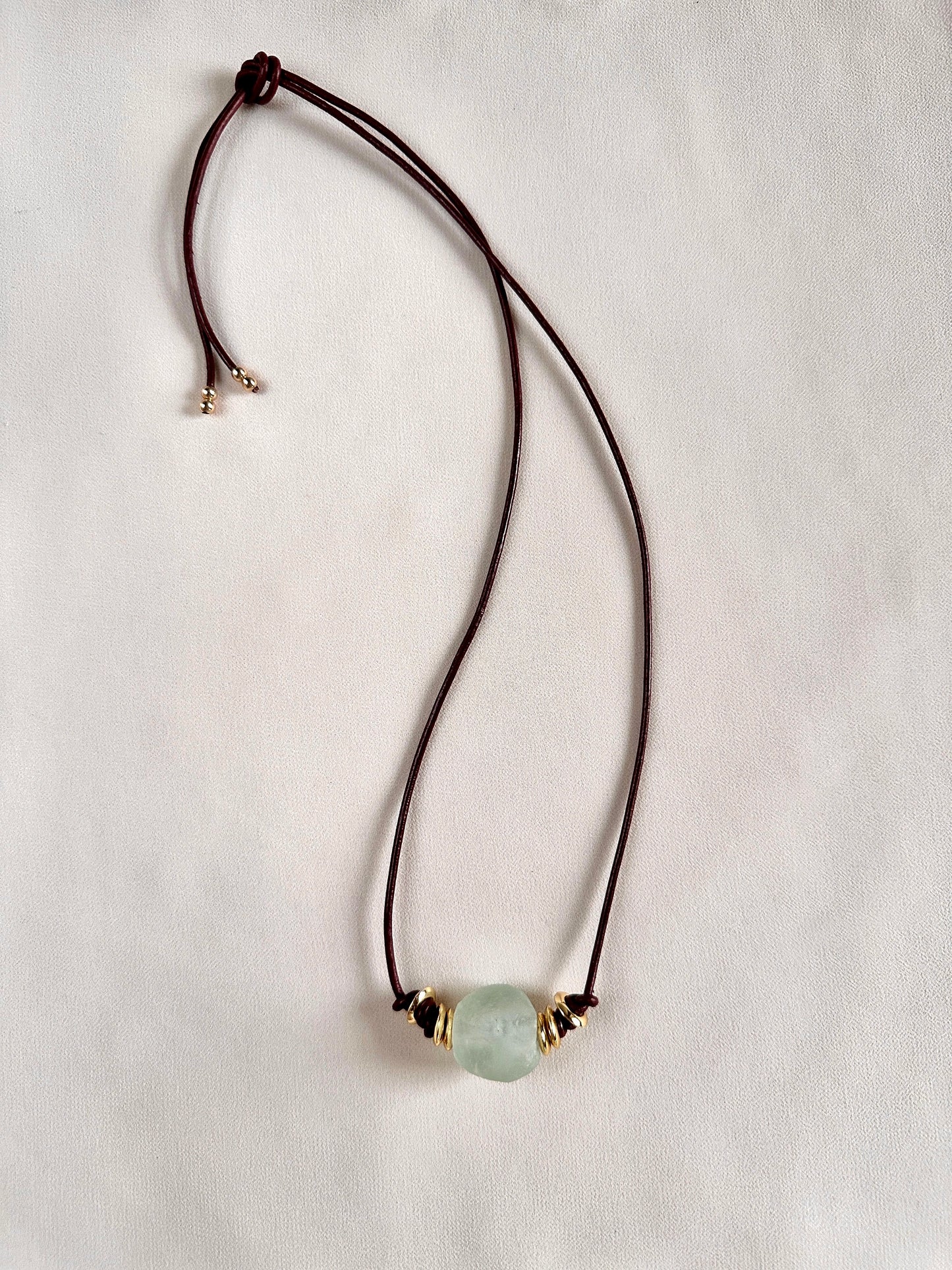 Leather burgundy necklace with a sea glass green bead on a white background