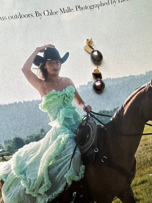 Magazine editorial of a woman in a green dress with a horse and a flat lay of dark pearl earrings on top. 
