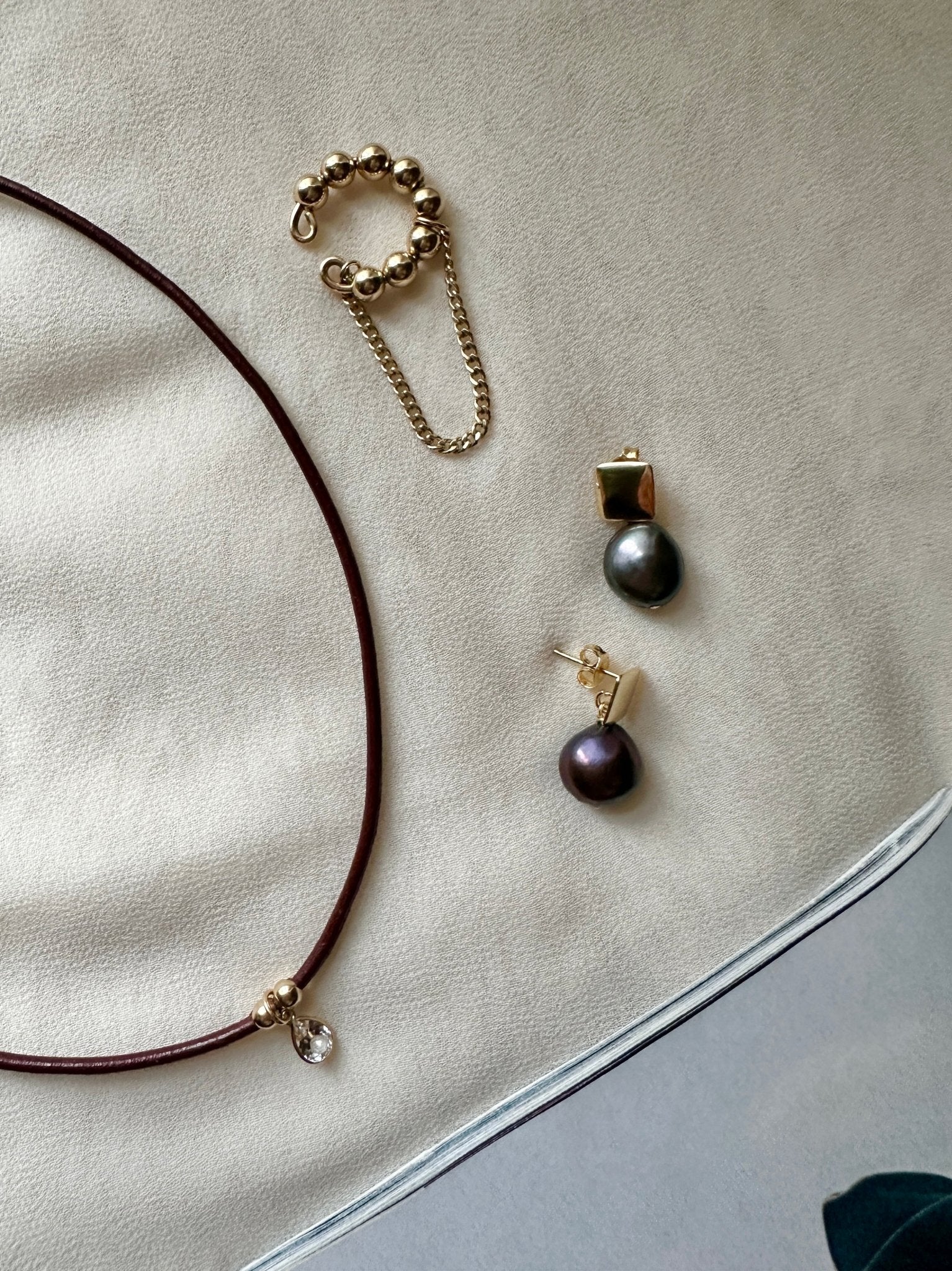 Jewelry set including a necklace, bracelet, and dark pearls earrings on a light fabric background