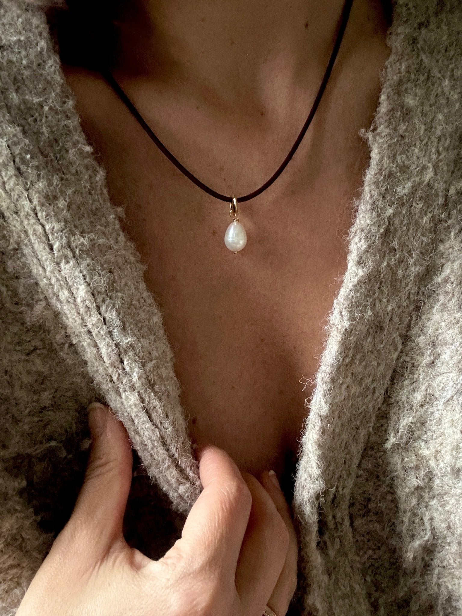 Person wearing a freshwater pearl pendant with gold-toned loop detail on a leather cord