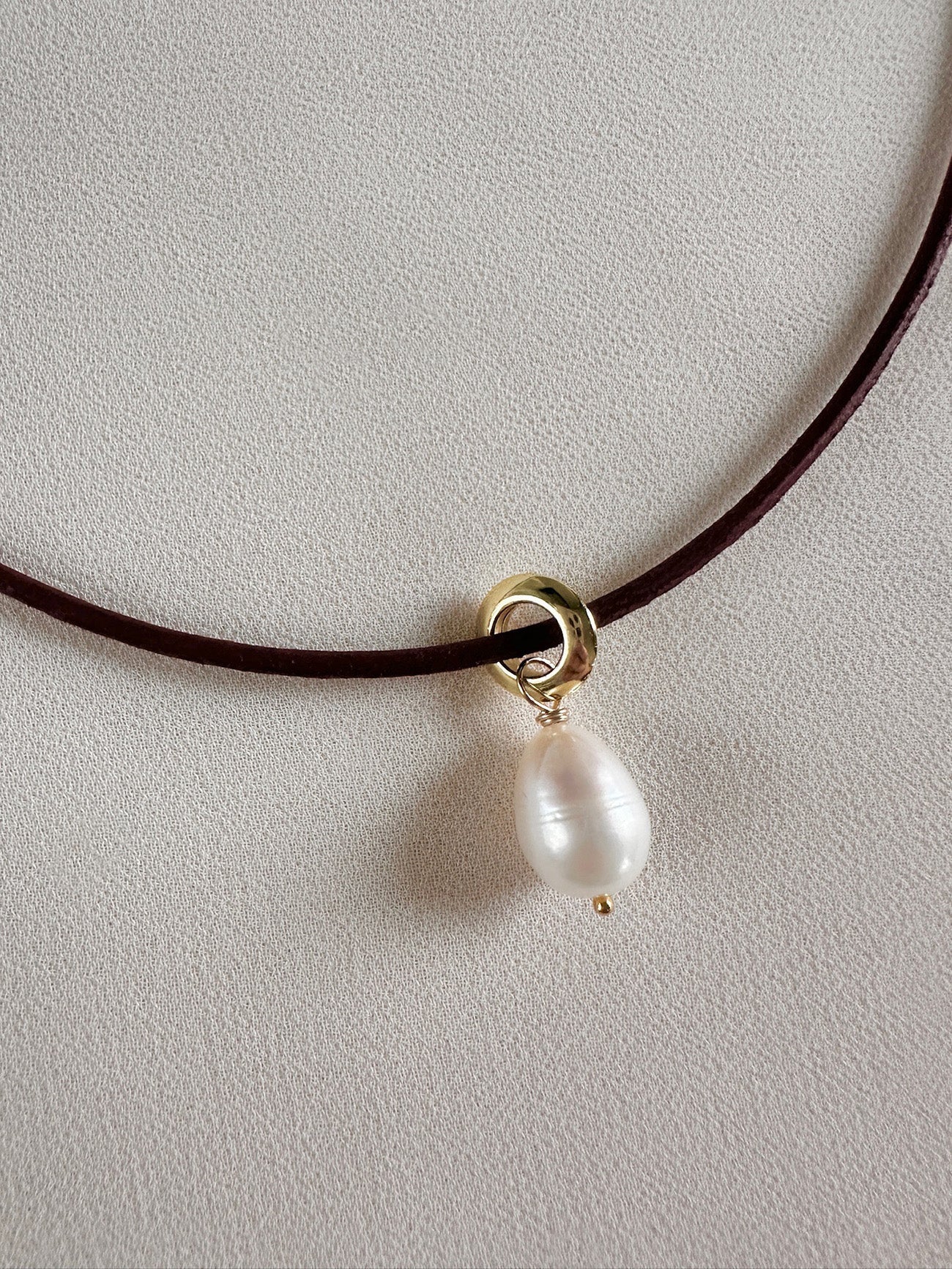 Minimal pearl necklace on leather cord laid on a white background
