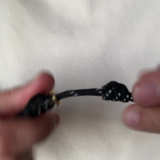 Video of a person demonstrating how to open and adjust a black paracord necklace with a pearl pendant.