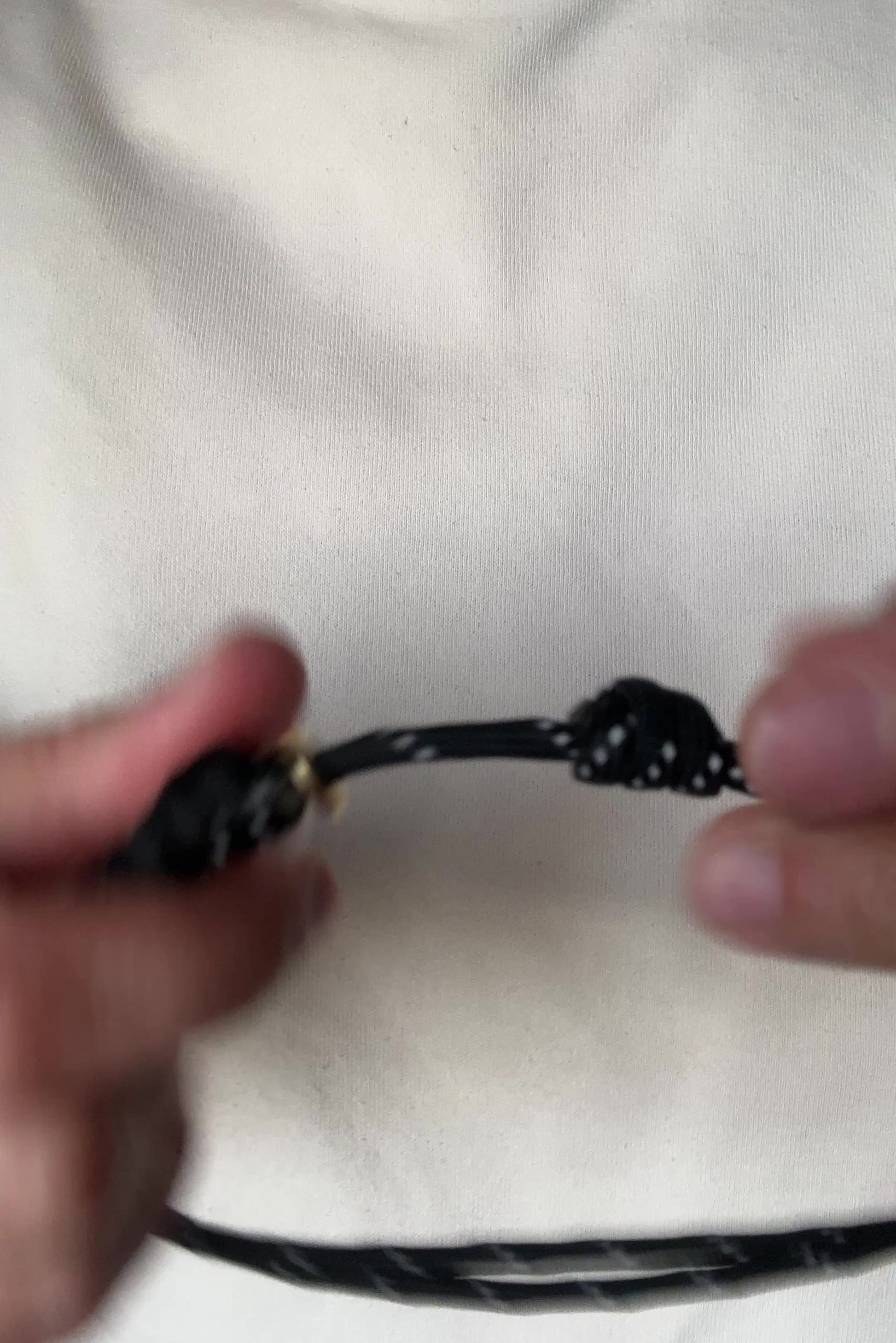 Video of a person demonstrating how to open and adjust a black paracord necklace with a pearl pendant.