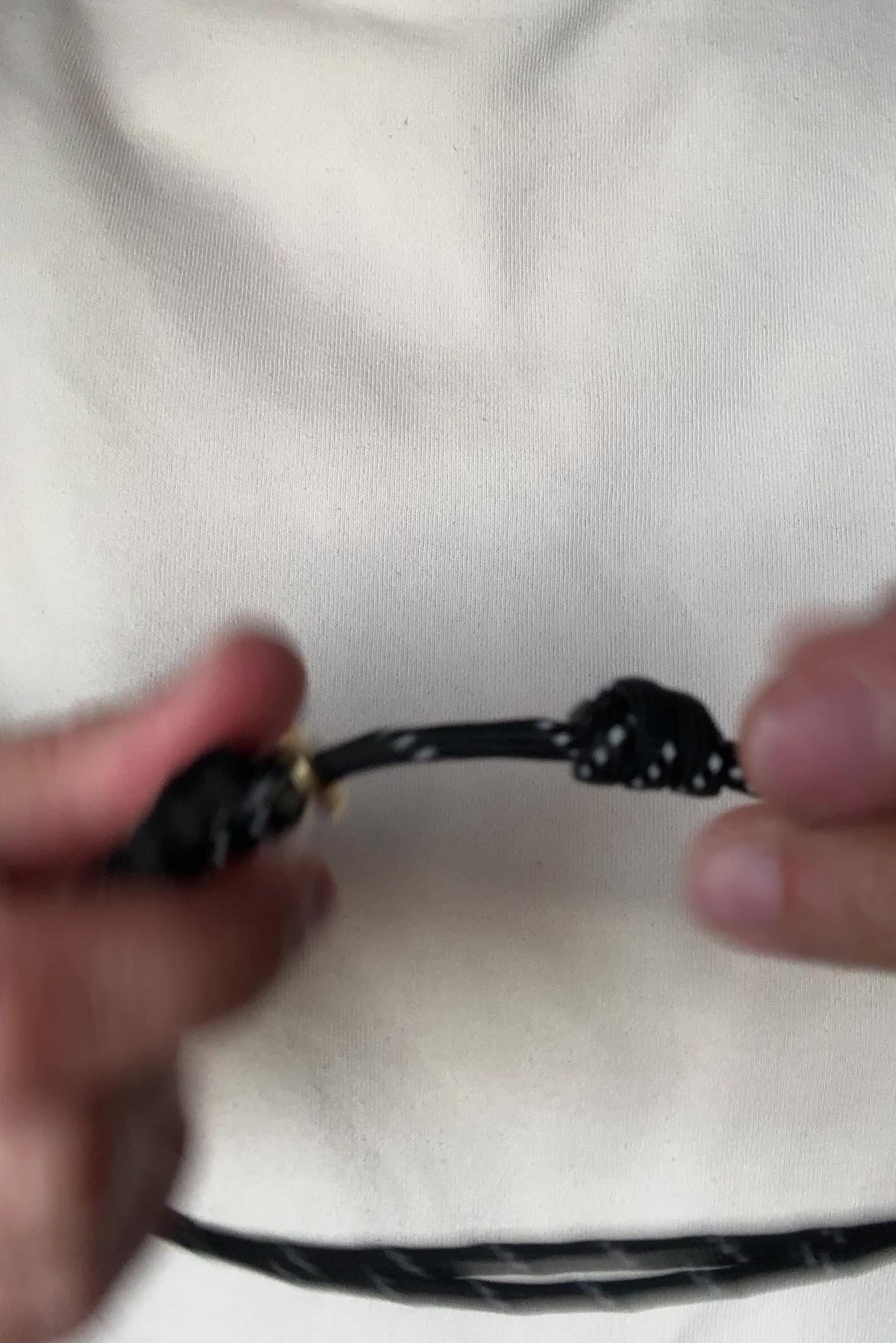 Video of a person demonstrating how to open and adjust a black paracord necklace with a pearl pendant.