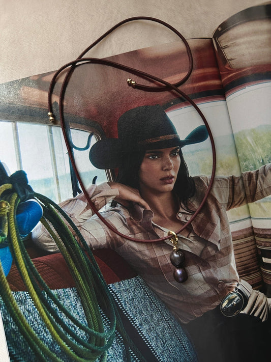 Red leather cord necklace with a dark double pearl pendant on a magazine spread.