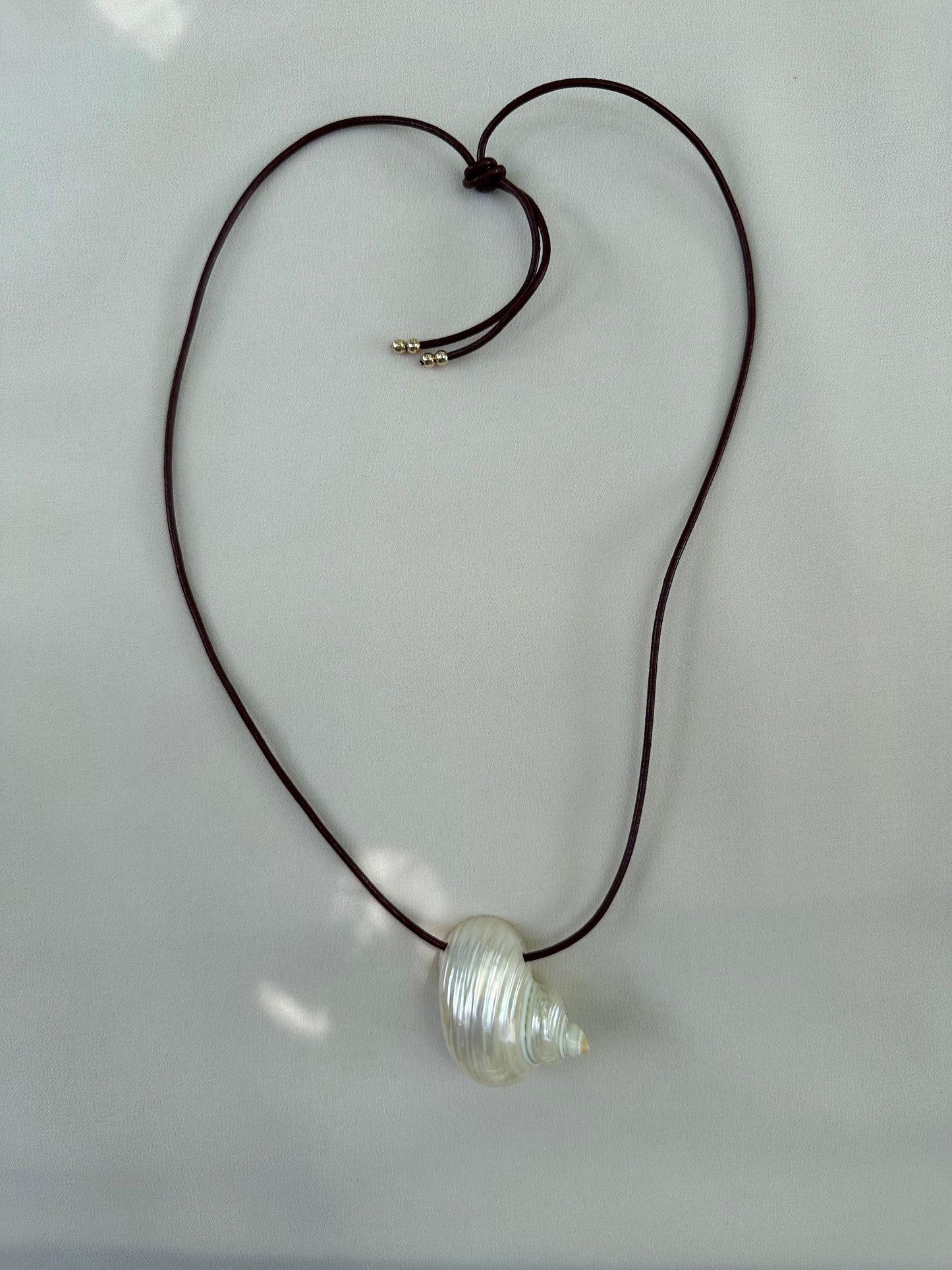 Natural shell necklace on burgundy leather cord flatlay on white packground and sun highlights
