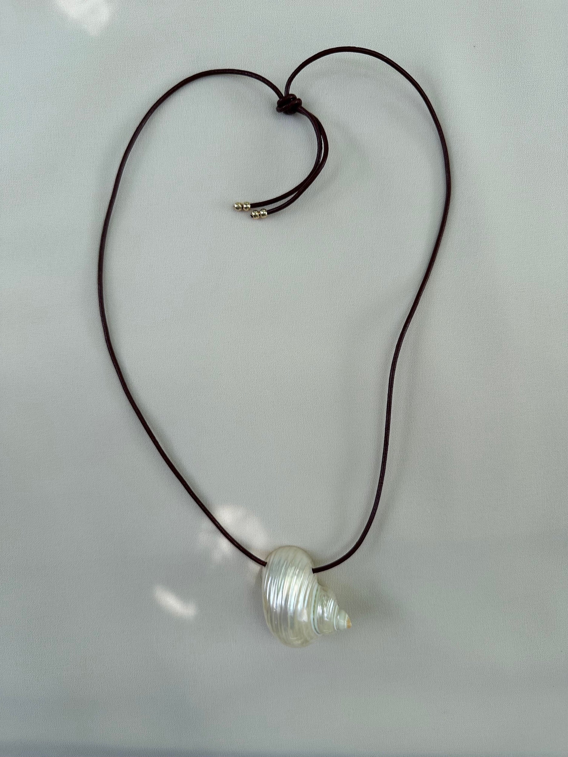 Natural shell necklace on burgundy leather cord flatlay on white packground and sun highlights
