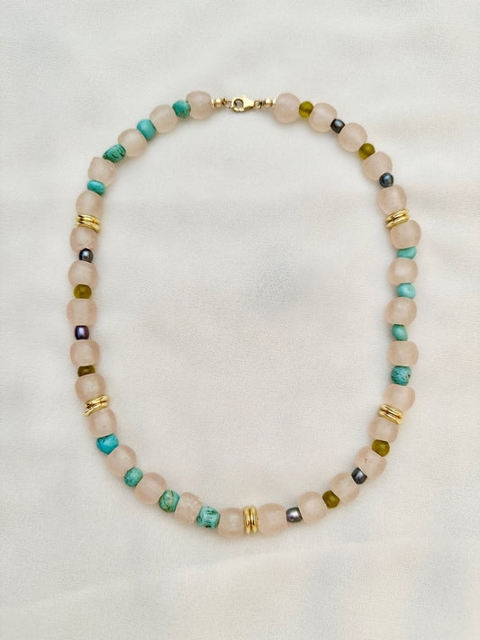 A beaded necklace with a mix of pearls, glass, stones, and gold plated details, displayed against a white background.